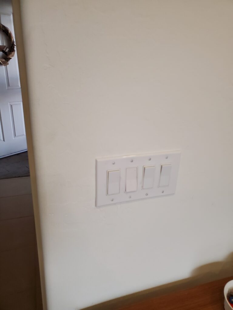 Four decorator light switches under one white cover plate on an interior wall